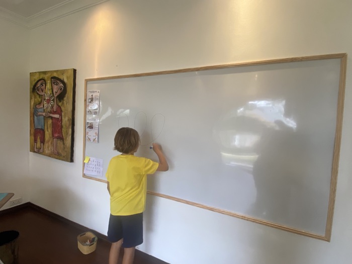 Un enfant trace au feutre sur le grand tableau blanc